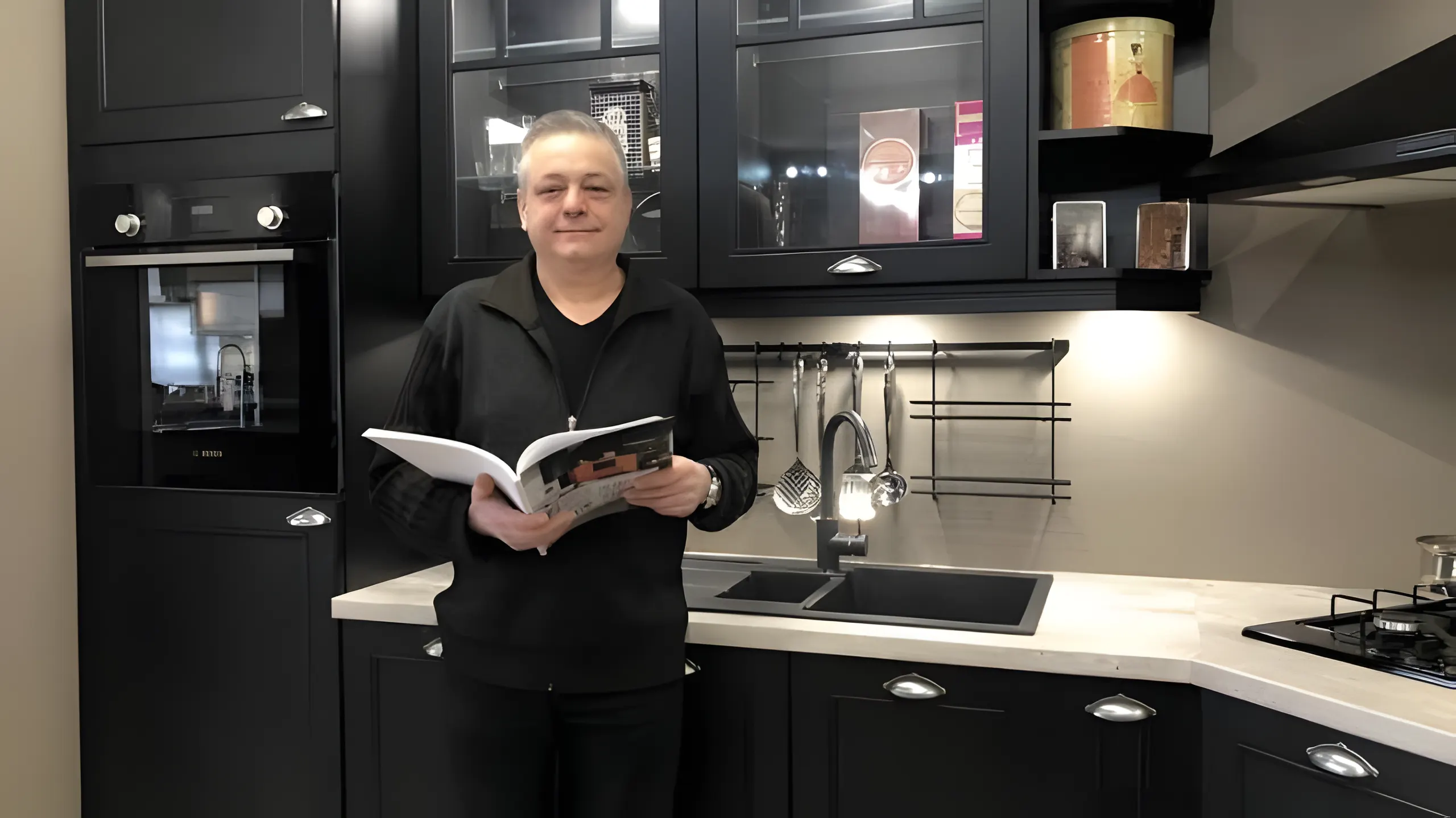 Rosario Giglio, gérant de Cuisines Giros, un catalogue ouvert dans les mains, devant une cuisine noire