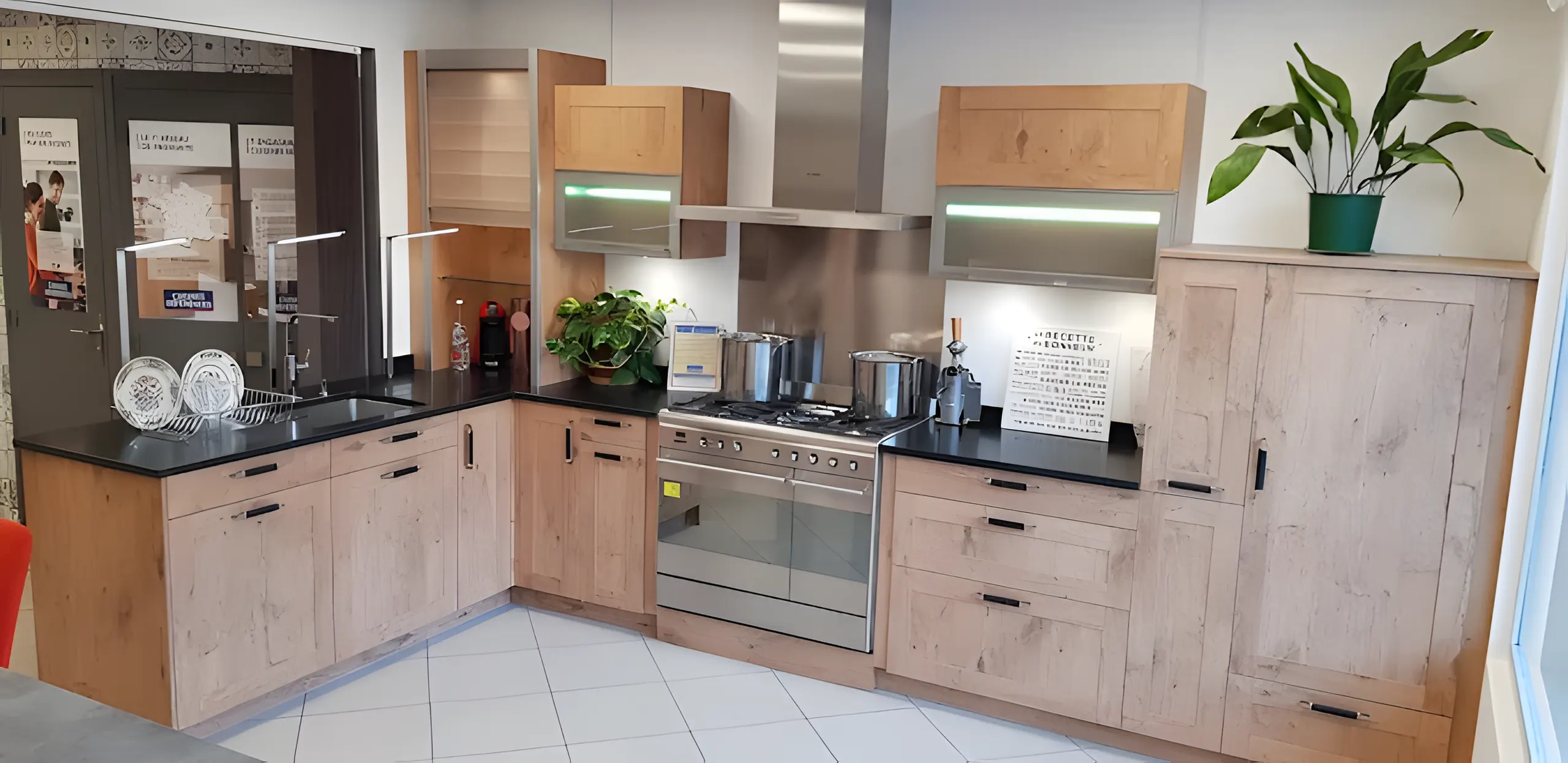 Cuisine exposée au showroom : façades en bois clair, plan noir et piano de cuisson en inox